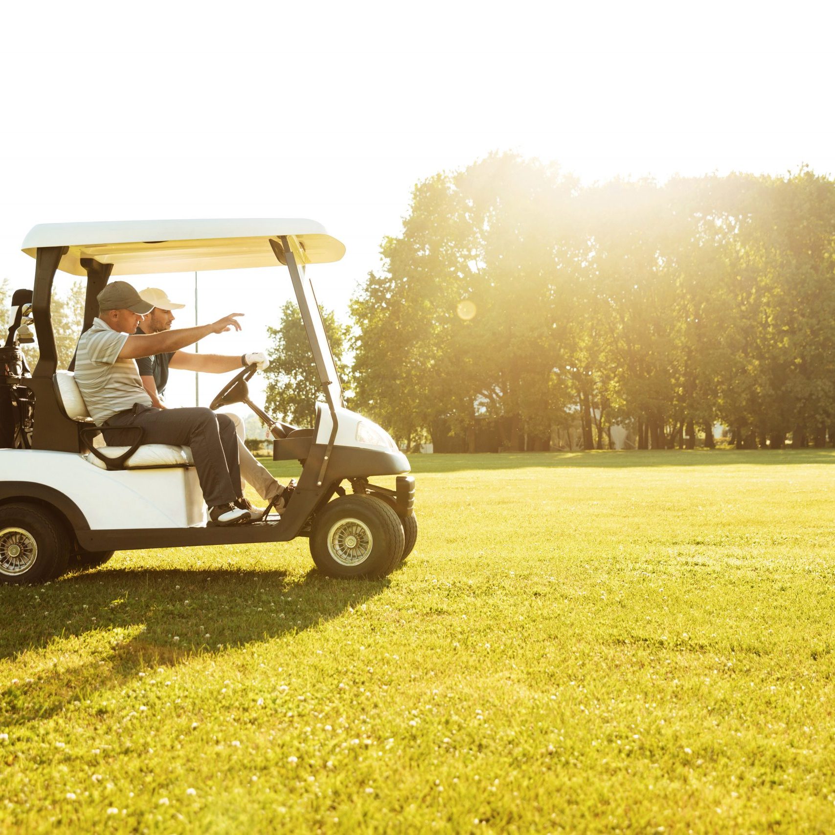 Two male golfers driving in a golf cart along green course